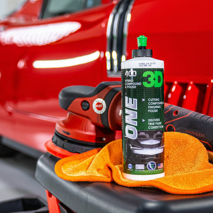 Car detailing tools and a bottle of 3D One product on a car surface with a red car in the background.