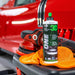 Car detailing tools and a bottle of 3D One product on a car surface with a red car in the background.